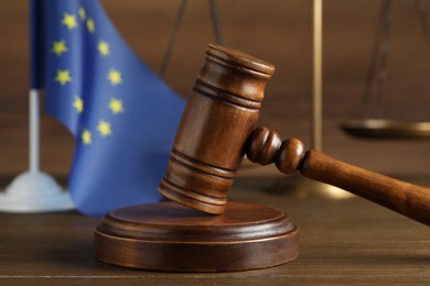 Photo of Judge's gavel, scales of justice and European Union flag on wooden table, closeup