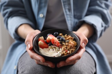 Photo of Woman holding bowl of tasty granola with berries, yogurt and seeds, closeup