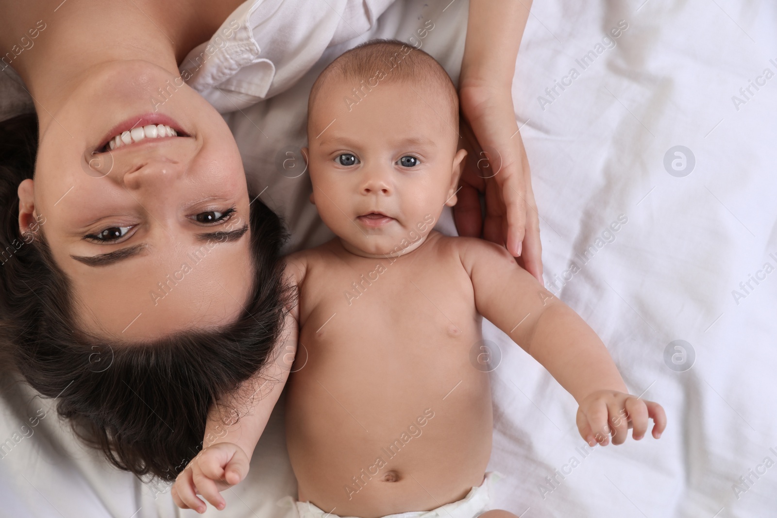 Photo of Happy young mother with her cute baby on bed, top view