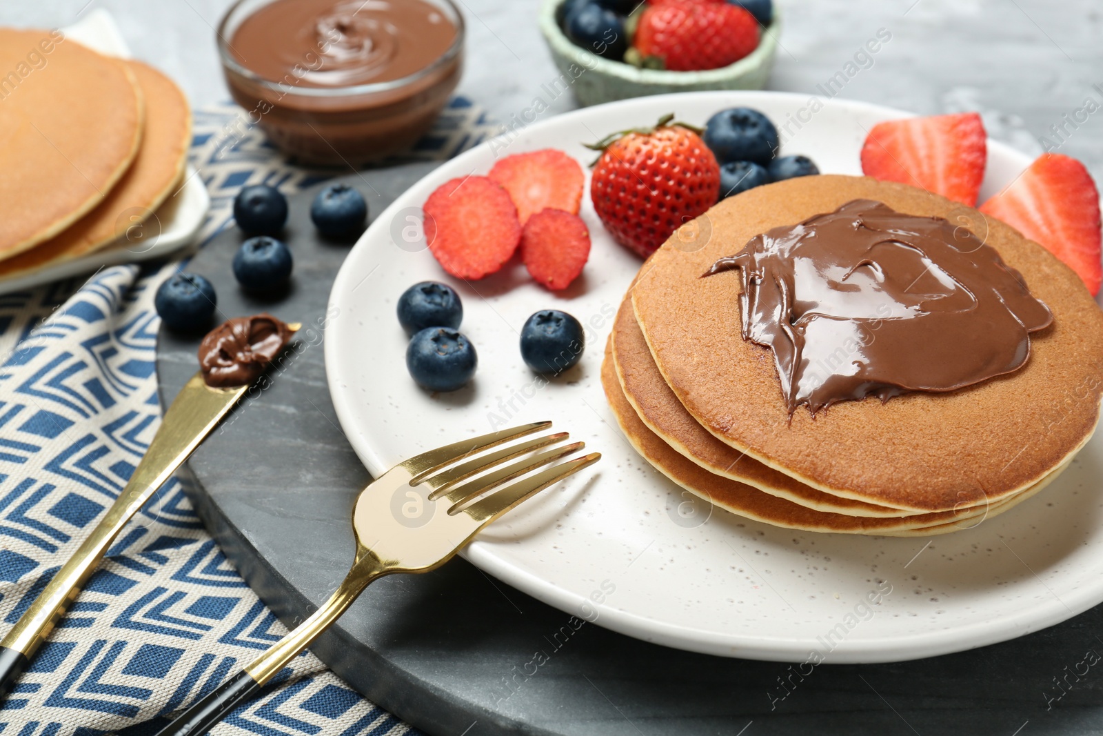 Photo of Tasty pancakes with chocolate paste and berries served on table, closeup