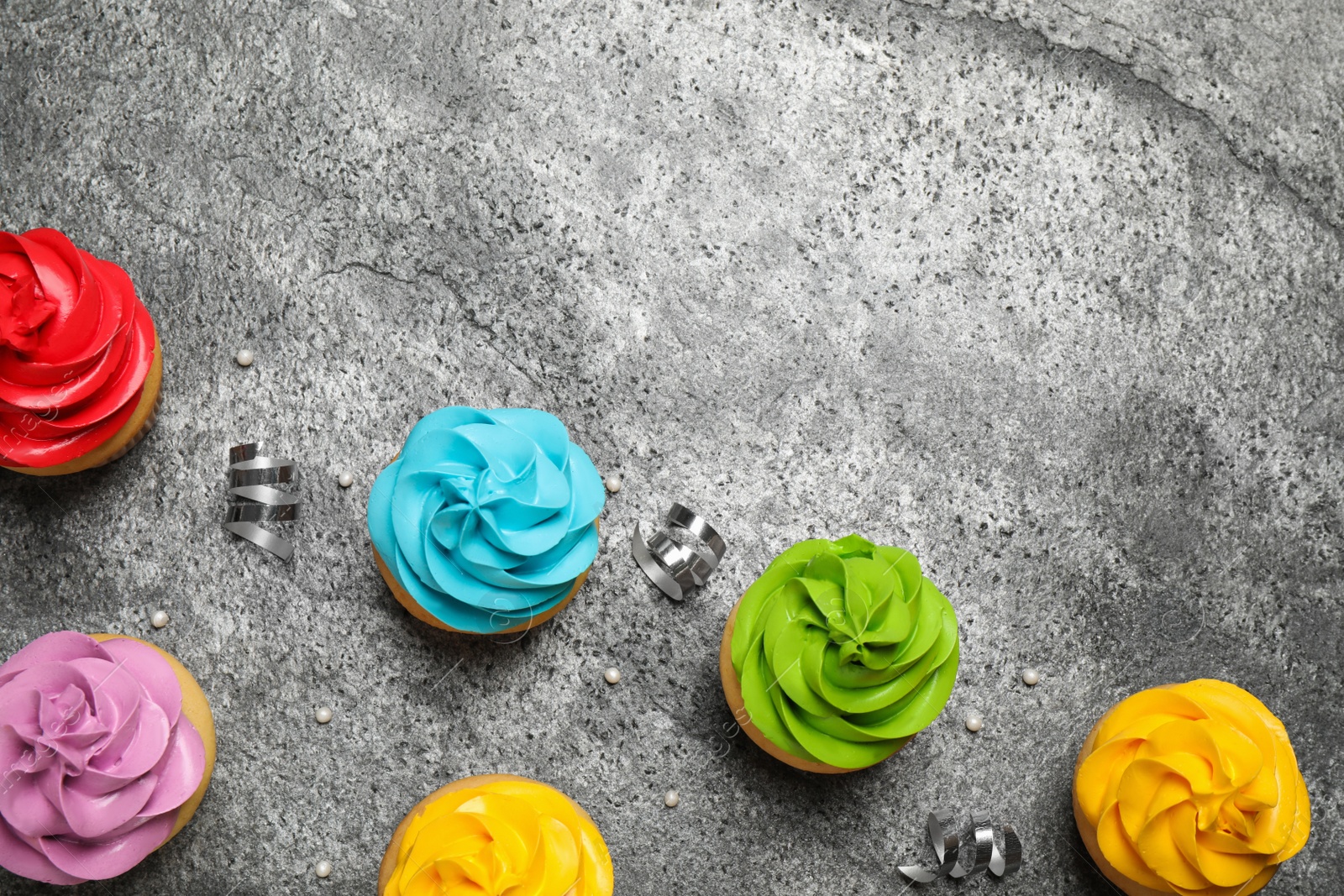 Photo of Flat lay composition with colorful birthday cupcakes on grey table. Space for text