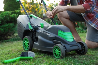 Man with screwdriver fixing lawn mower in garden, closeup