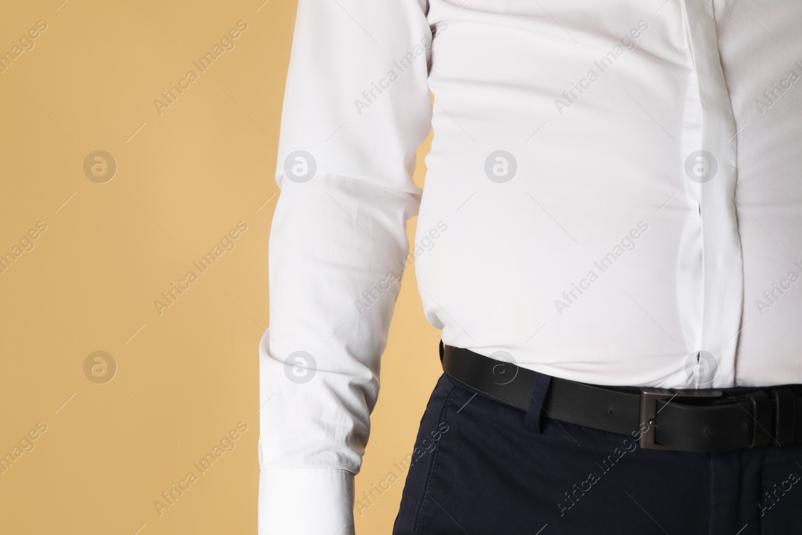 Photo of Overweight man in tight shirt on yellow background, closeup. Space for text