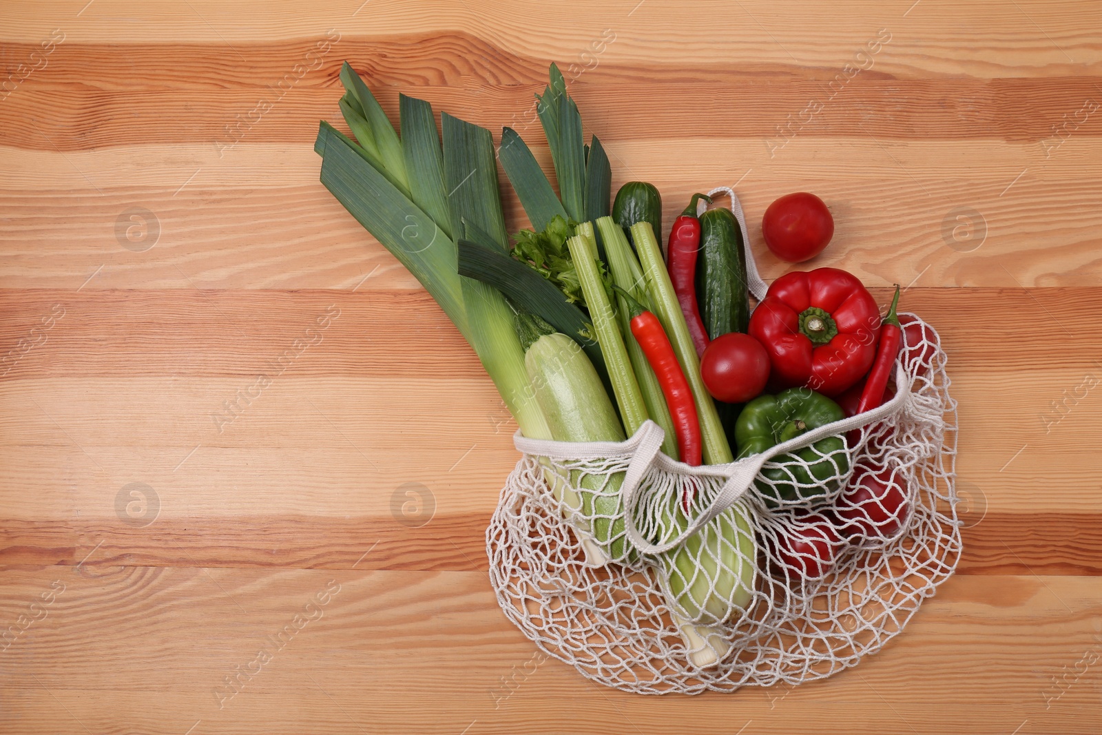 Photo of Net bag with vegetables on wooden background, top view