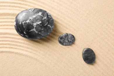 Photo of Zen garden stones on beige sand with pattern, flat lay