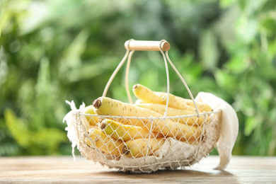 Photo of Raw white carrots in basket on wooden table against blurred background