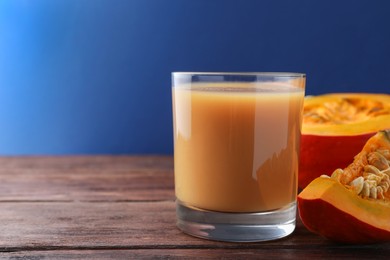 Tasty pumpkin juice in glass and cut pumpkin on wooden table against blue background. Space for text