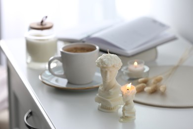 Photo of Beautiful David bust candles and cup of hot drink on  white table indoors, space for text