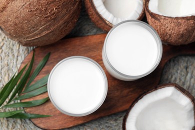 Glasses of delicious coconut milk, palm leaf and coconuts on table, flat lay