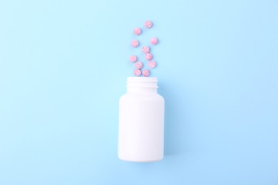 Photo of Jar with vitamin pills on light blue background, top view