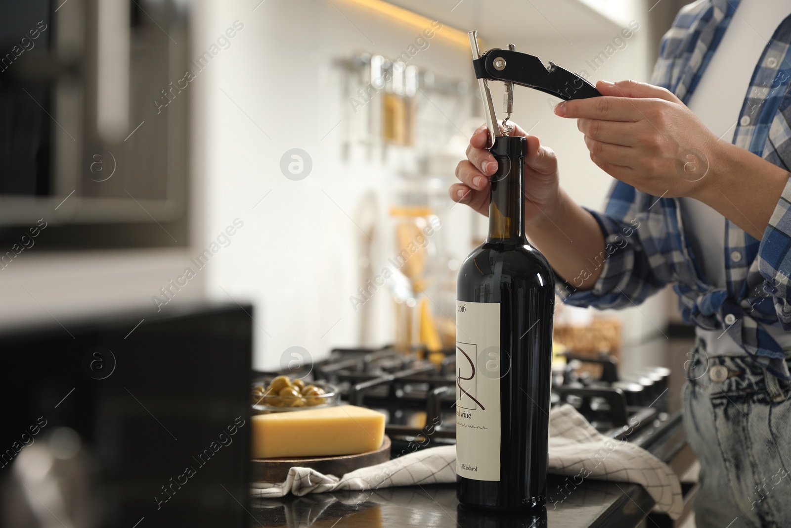 Photo of Woman opening wine bottle with corkscrew at black countertop indoors, closeup