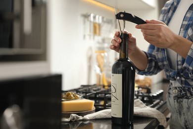 Photo of Woman opening wine bottle with corkscrew at black countertop indoors, closeup