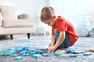 Photo of Cute little child playing with puzzles on floor indoors