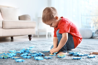 Cute little child playing with puzzles on floor indoors