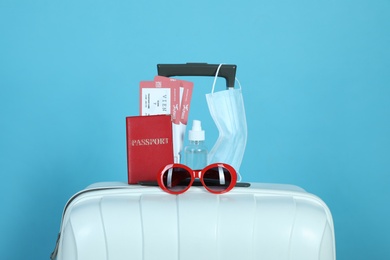 Photo of Composition with passport and protective mask on suitcase against light blue background. Travel during quarantine