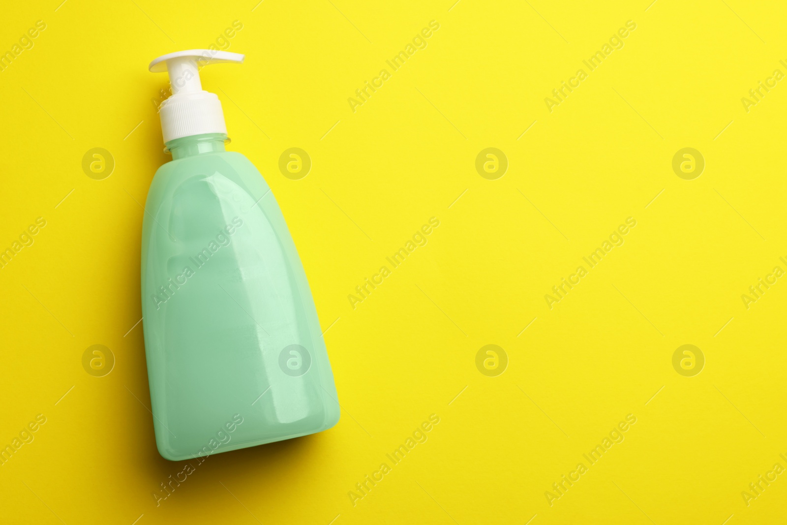 Photo of Bottle of liquid soap on yellow background, top view. Space for text