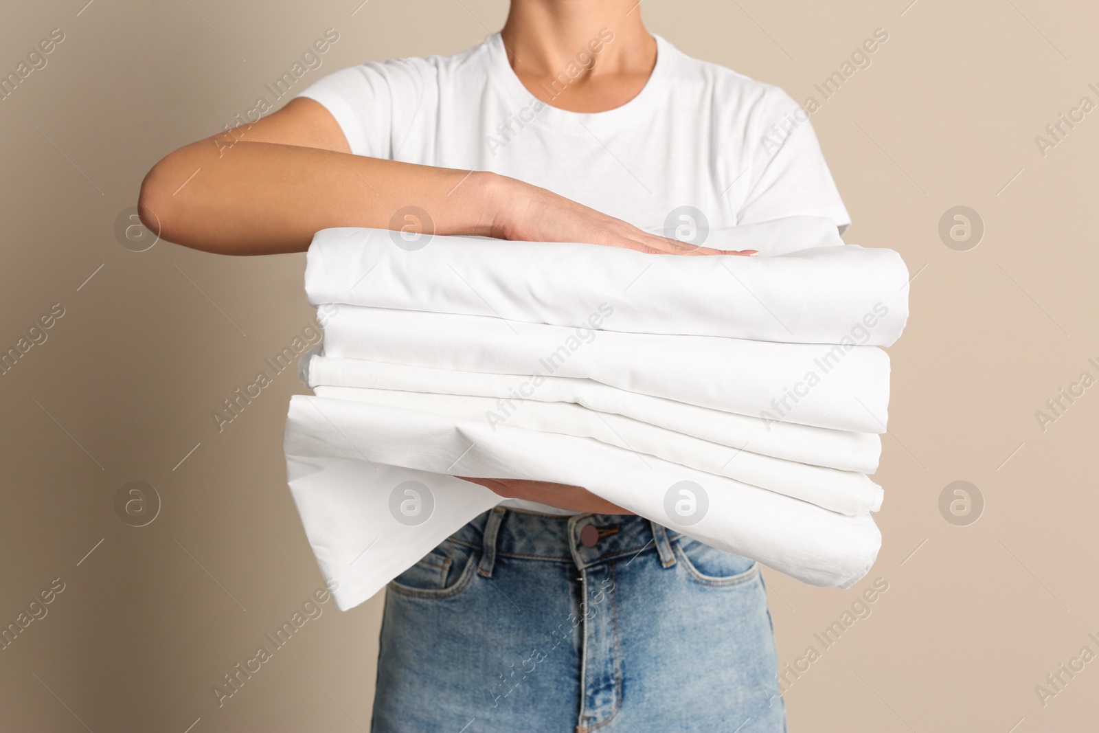 Photo of Woman holding stack of clean bed linens on beige background