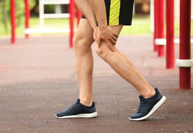 Photo of Young man suffering from knee pain on sports ground, closeup