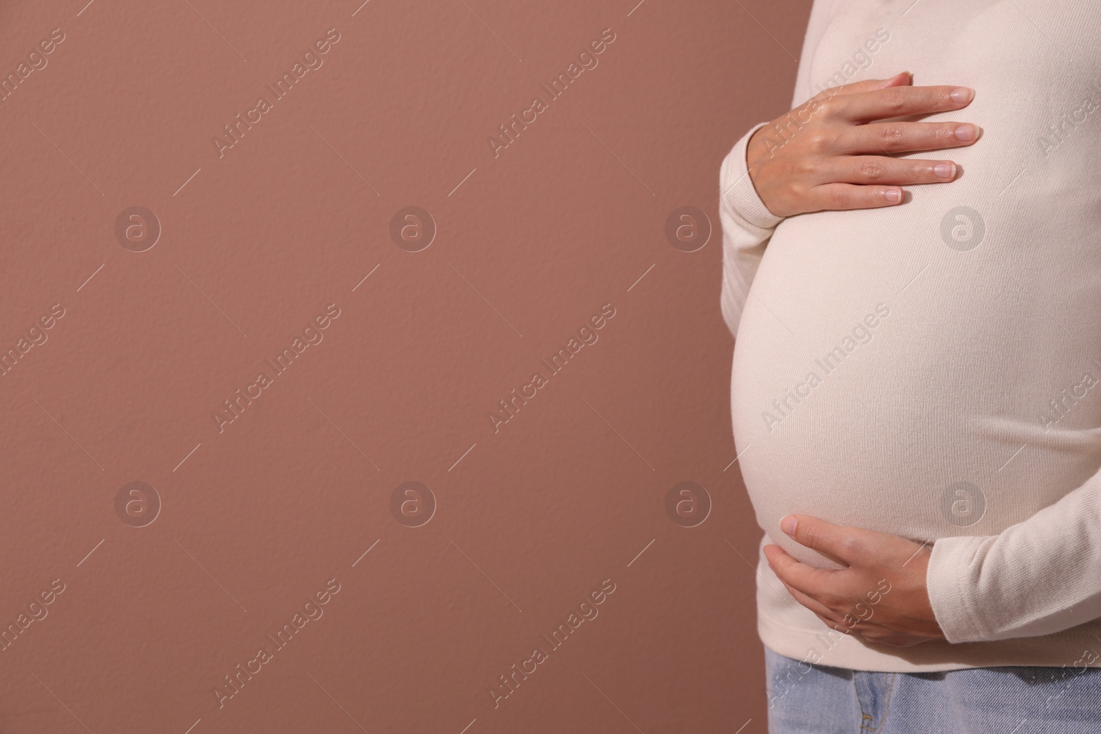 Photo of Pregnant young African-American woman on dusty rose background, closeup. Space for text