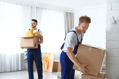 Photo of Moving service employees with cardboard boxes in room