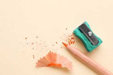 Photo of Orange pencil, sharpener and shavings on beige background, flat lay. Space for text