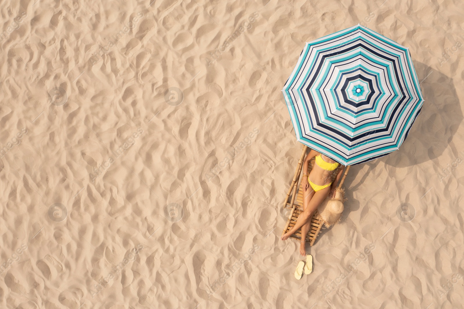 Image of Woman resting in sunbed under striped beach umbrella at sandy coast, aerial view. Space for text