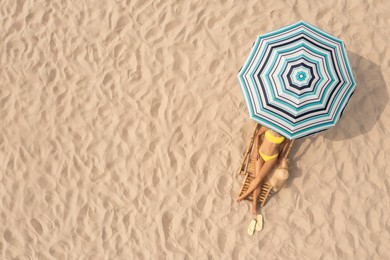 Image of Woman resting in sunbed under striped beach umbrella at sandy coast, aerial view. Space for text