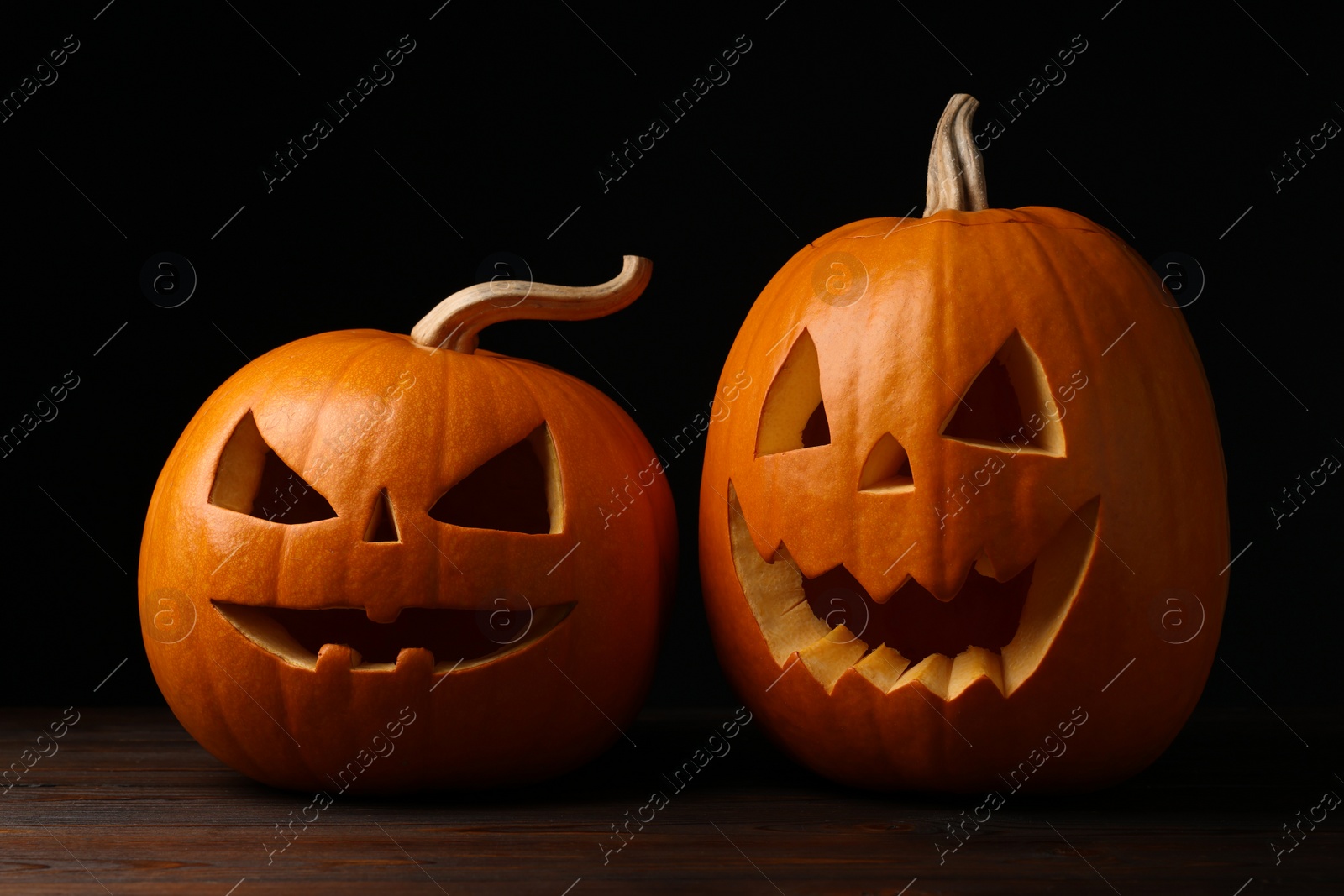 Photo of Scary jack o'lanterns made of pumpkins on wooden table in darkness. Halloween traditional decor