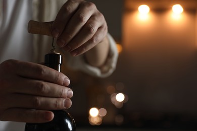 Photo of Man opening wine bottle with corkscrew on blurred background, closeup. Space for text