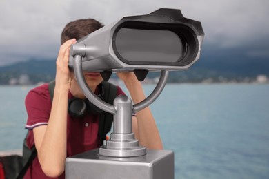 Photo of Teenage boy looking through mounted binoculars near sea, closeup. Space for text