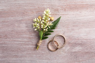 Small stylish boutonniere and rings on light wooden table, top view