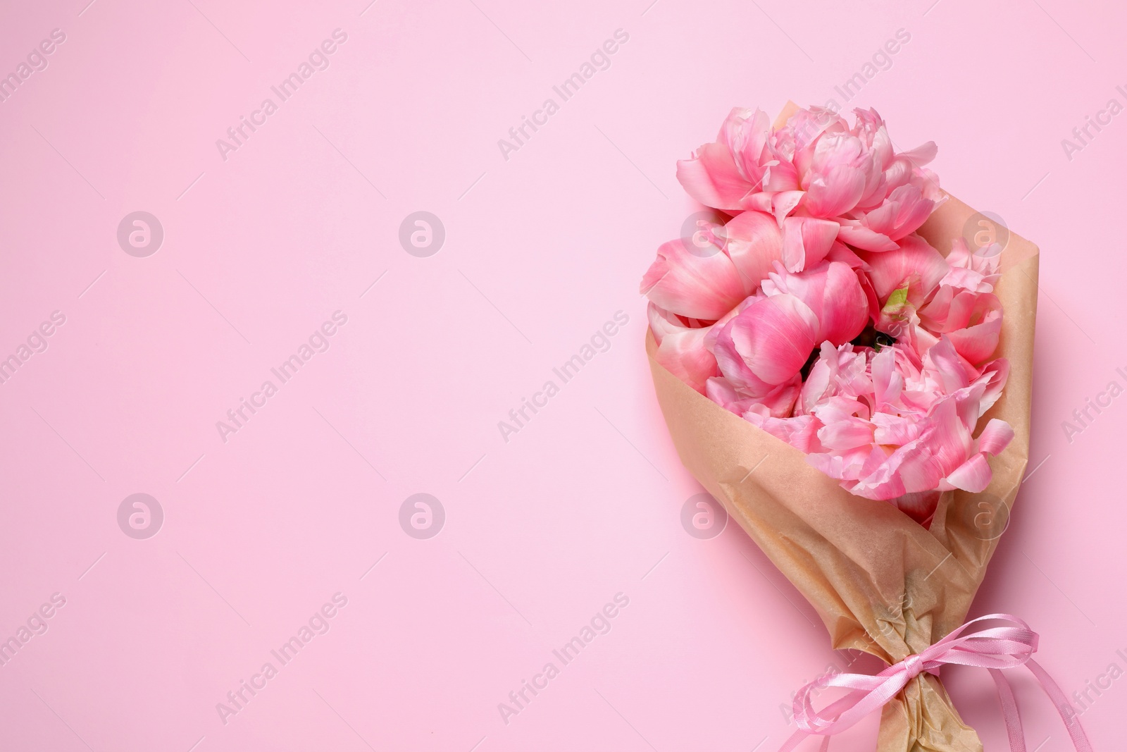 Photo of Beautiful bouquet of peonies wrapped in paper on pink background, top view. Space for text