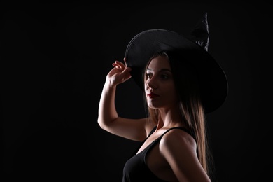Photo of Young woman wearing witch costume on black background, space for text. Halloween party