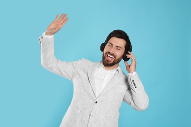 Photo of Happy man listening music with headphones on light blue background