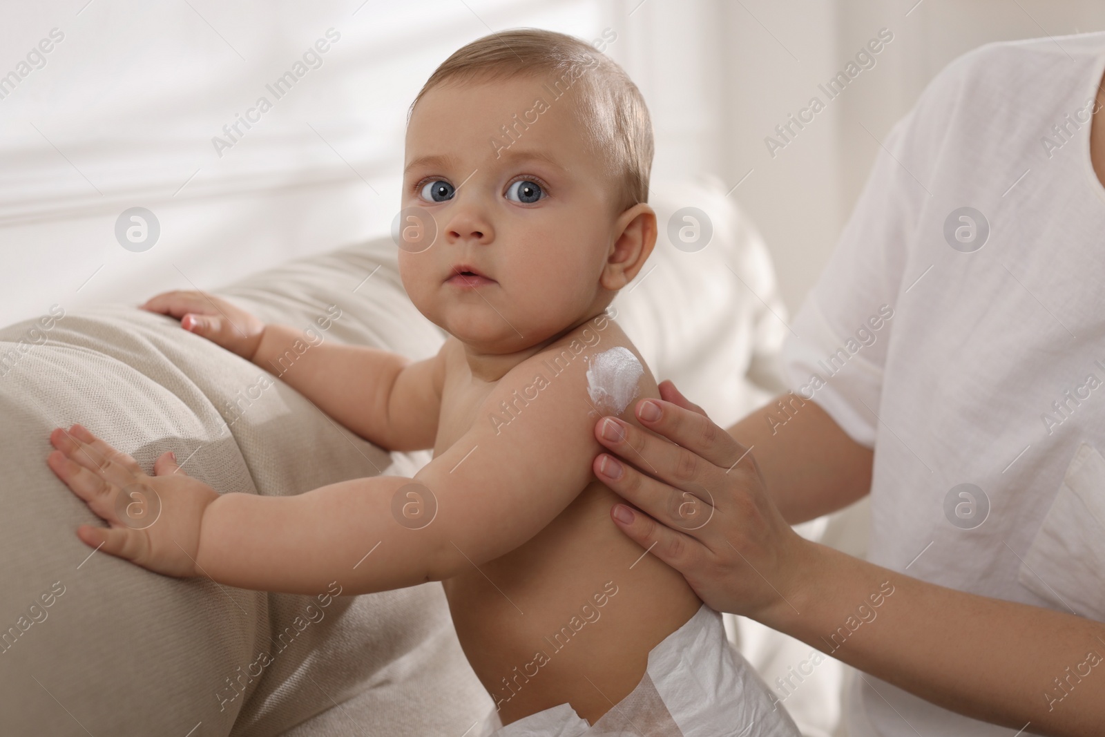 Photo of Mother applying body cream on her little baby at home, closeup