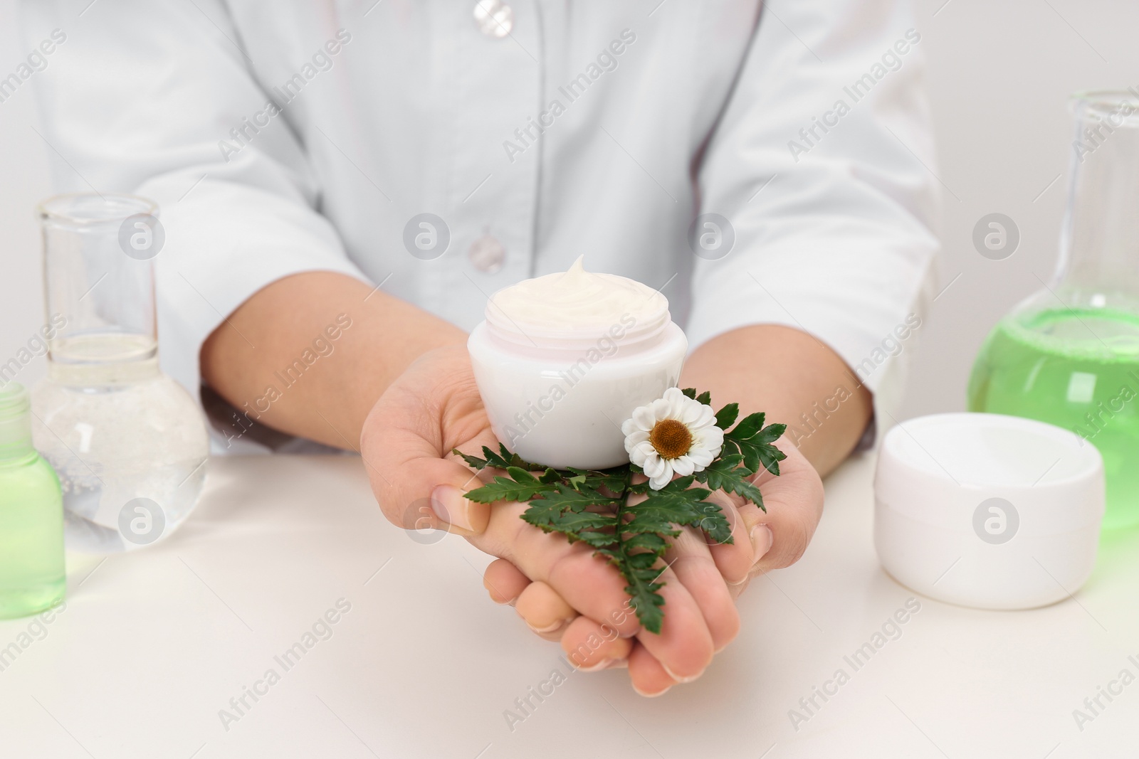 Photo of Female dermatologist holding jar of skin care product at table, closeup