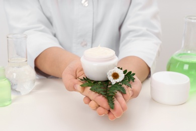 Photo of Female dermatologist holding jar of skin care product at table, closeup