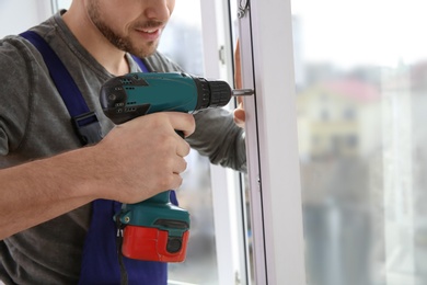 Photo of Construction worker using drill while installing window indoors, closeup
