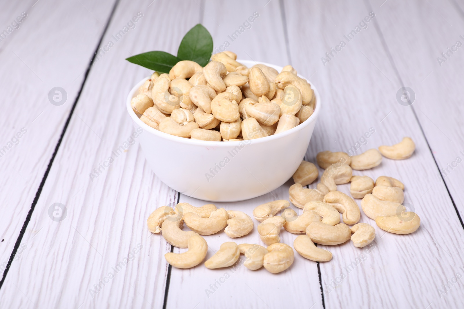 Photo of Tasty cashew nuts and green leaves on white wooden table