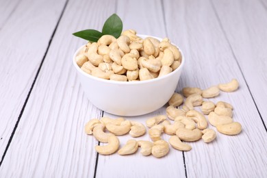 Photo of Tasty cashew nuts and green leaves on white wooden table