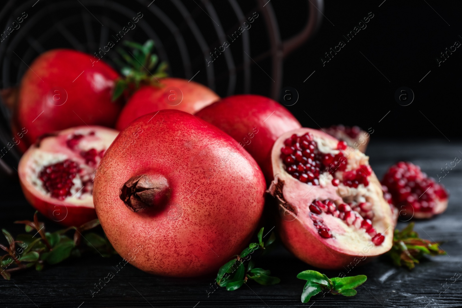 Photo of Delicious ripe pomegranates on black wooden table, closeup