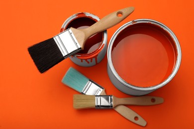 Cans of orange paint and brushes on color background, flat lay