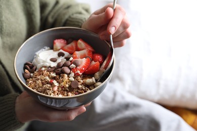 Woman eating tasty granola with chocolate chips, strawberries and yogurt indoors, closeup. Space for text