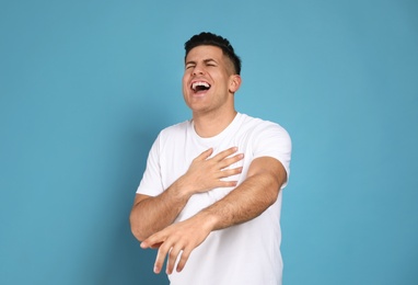 Handsome man laughing on light blue background. Funny joke