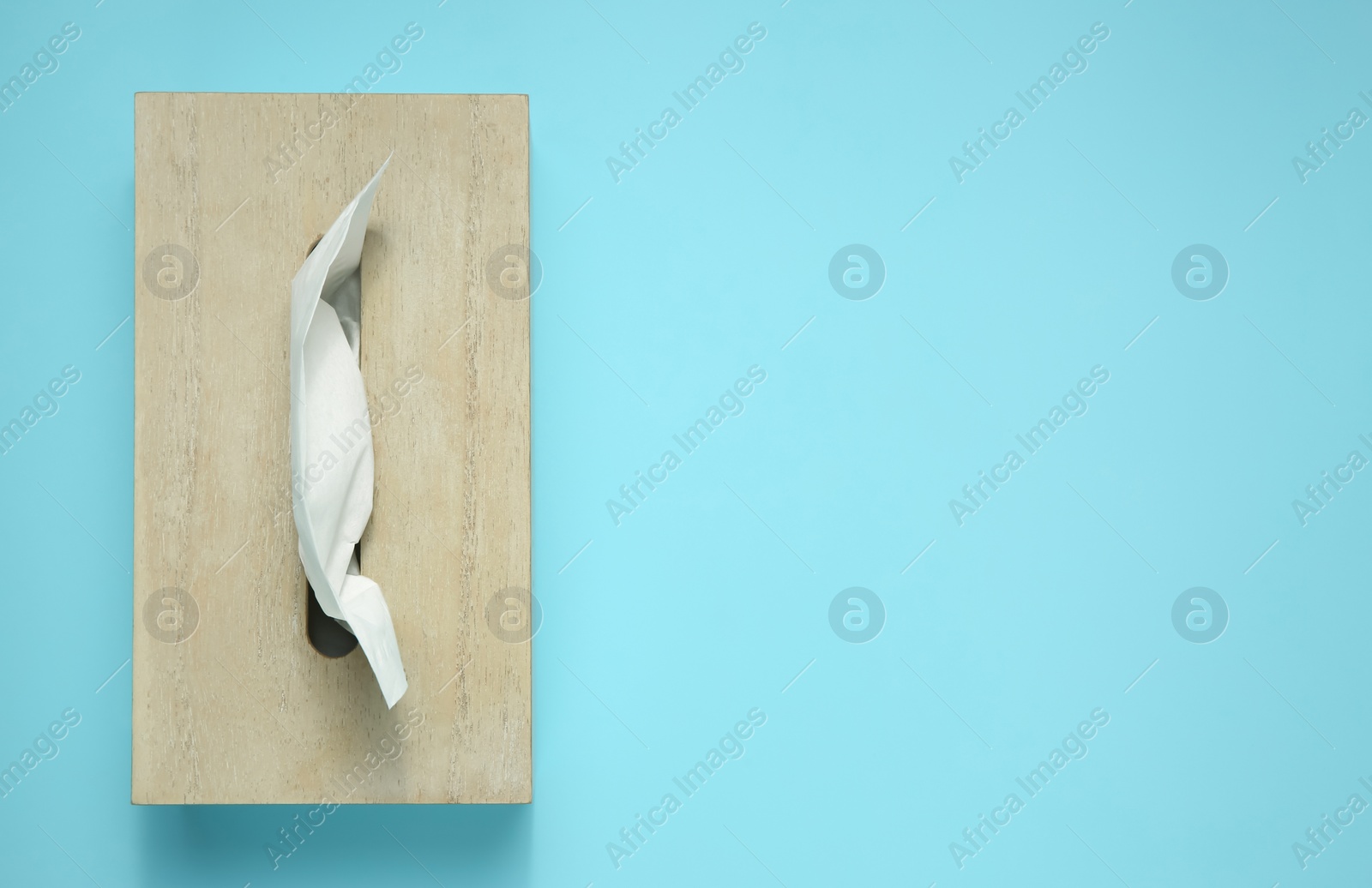 Photo of Wooden holder with paper tissues on light blue background, top view. Space for text