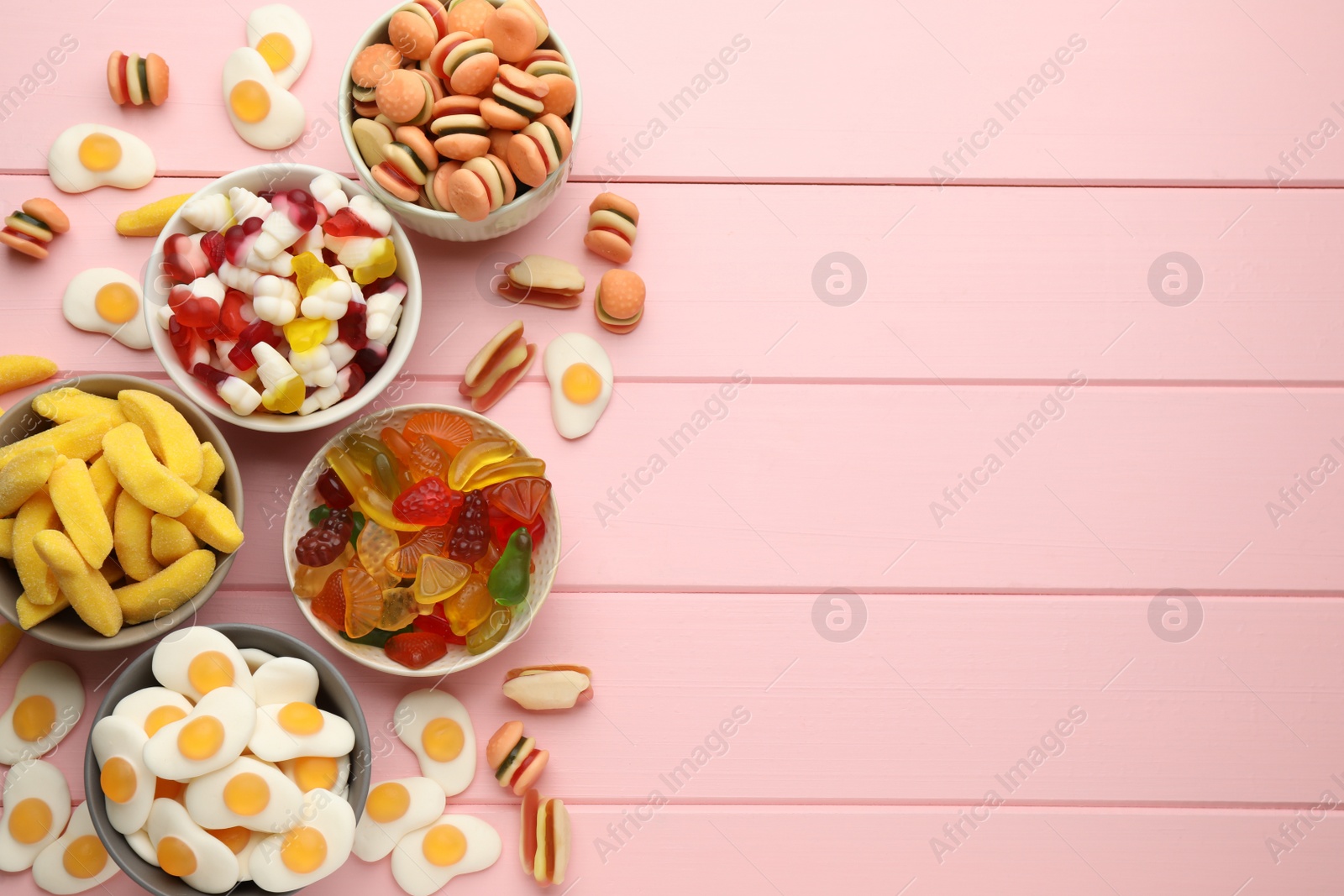 Photo of Many different delicious gummy candies on pink wooden table, flat lay. Space for text