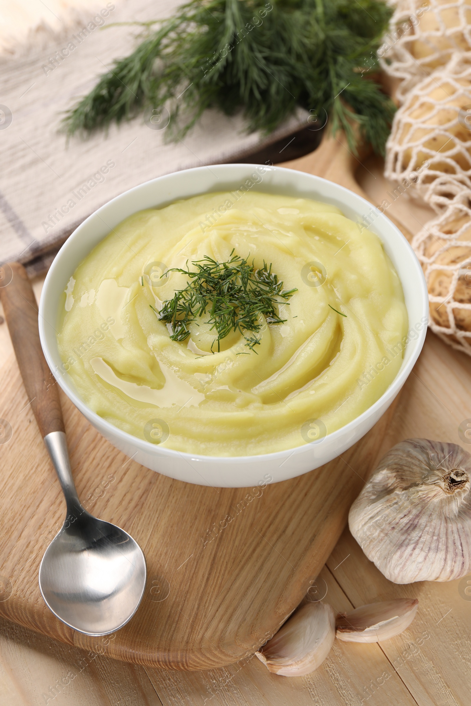 Photo of Bowl of tasty cream soup with dill, spoon and garlic on wooden table