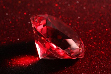 Photo of Beautiful shiny diamond on red glitter background, closeup