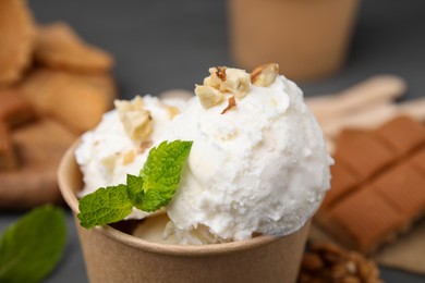 Photo of Tasty ice cream with mint and nuts in paper cup on table, closeup