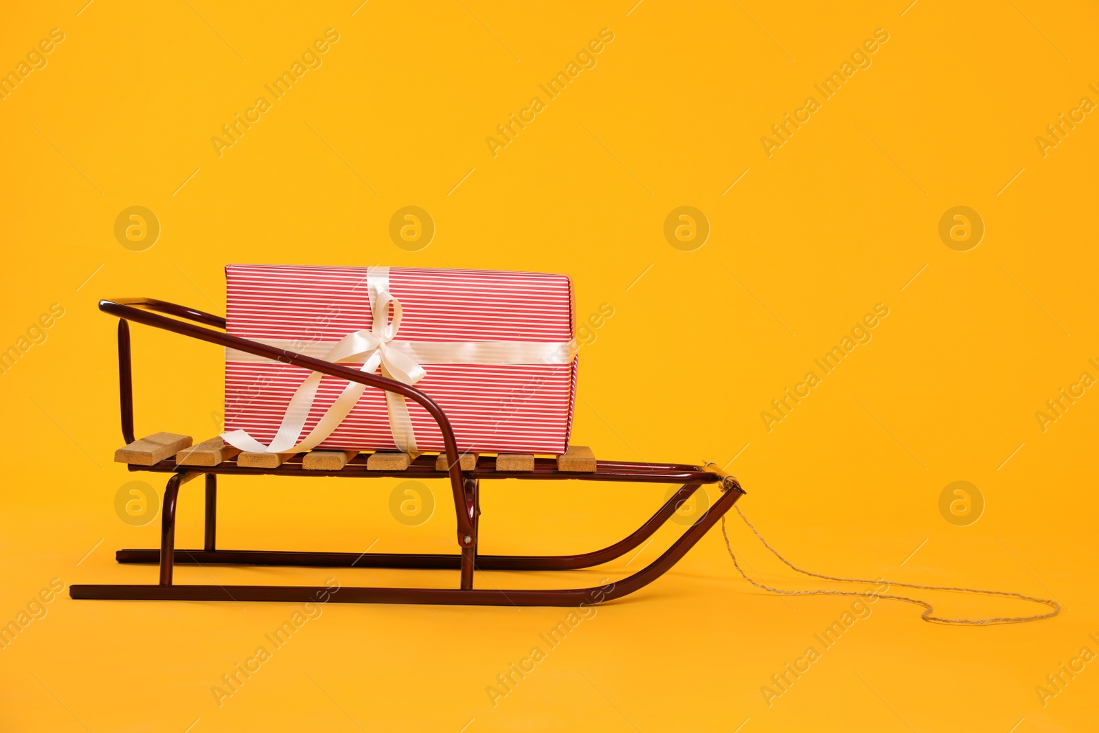 Photo of Stylish sleigh with Christmas gift on yellow background, space for text